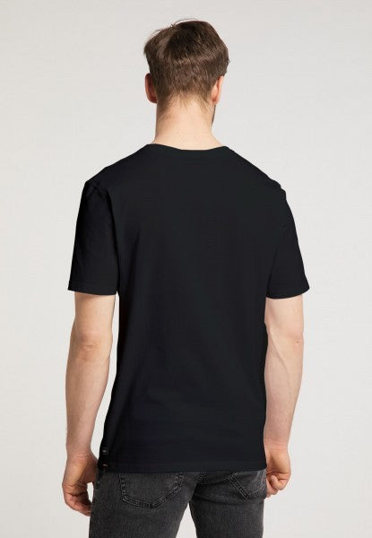 Ein Mann mit heller Haut und kurzen braunen Haaren steht mit dem Rücken zur Kamera und trägt das schlichte schwarze Recaro T-Shirt Spektrum und dunkle Jeans vor einem neutralen Hintergrund für einen dezenten Retro-Look.