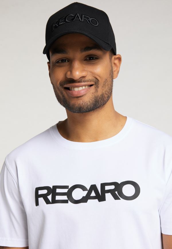 Ein lächelnder Mann trägt eine schwarze RECARO Baseball Cap Originals und ein weißes T-Shirt, beide mit kräftigem schwarzen Schriftzug. Ein heller Hintergrund hebt die stilvollen Ton-in-Ton-Stickerei-Details hervor.