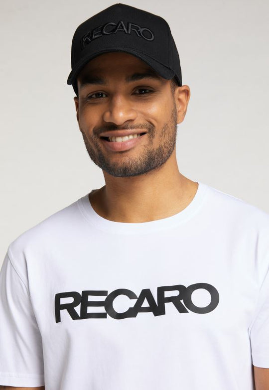 Ein lächelnder Mann trägt eine schwarze RECARO Baseball Cap Originals und ein weißes T-Shirt, beide mit kräftigem schwarzen Schriftzug. Ein heller Hintergrund hebt die stilvollen Ton-in-Ton-Stickerei-Details hervor.