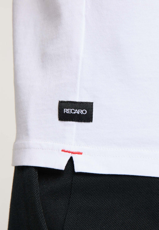 Nahaufnahme des unteren Teils eines T-Shirts Originals RECARO von Recaro_Merch_Daniel aus hochwertiger Baumwolle mit einem kleinen schwarzen „RECARO“-Etikett und roten Nähten über der schwarzen Hose.