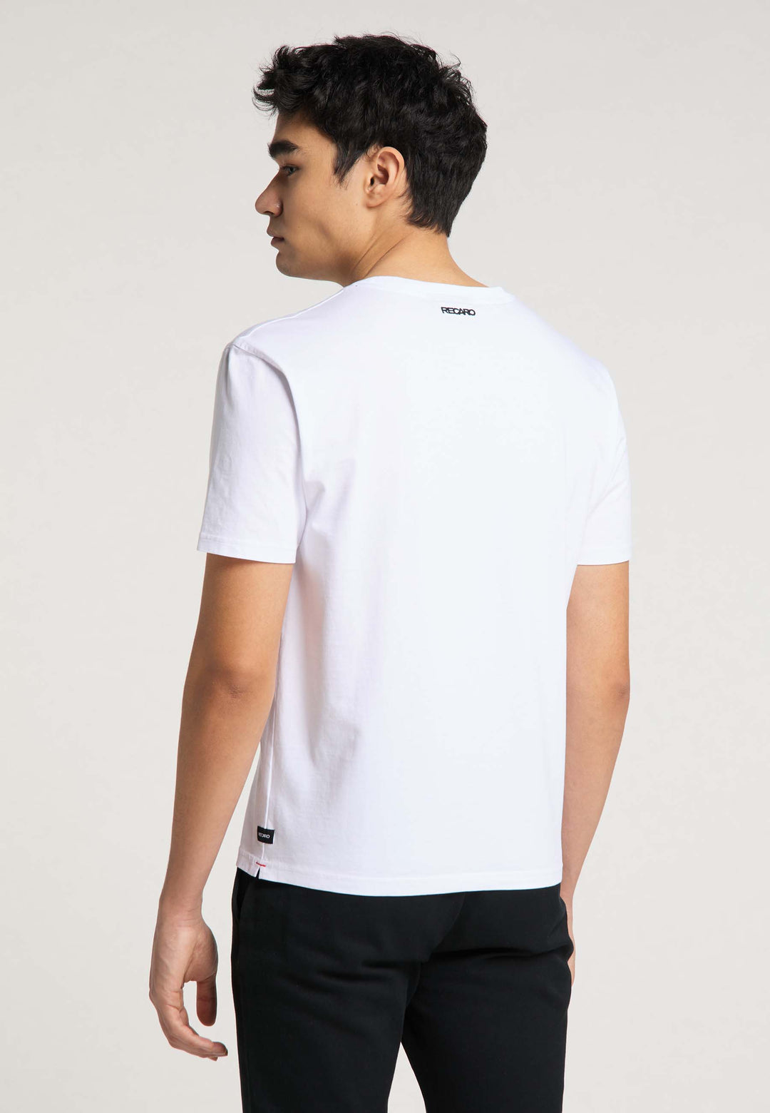 Ein junger Mann mit kurzen dunklen Haaren blickt von der Kamera weg und trägt ein T-Shirt Originals RECARO von Recaro_Merch_Daniel und eine schwarze Hose vor einem neutralen Hintergrund.