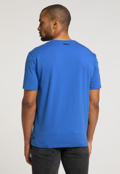 Von hinten ist ein Mann mit kurzen Haaren und Bart zu sehen, der ein leuchtend blaues Recaro_Merch_Daniel T-Shirt Originals RECARO in Regular Fit-Baumwolle und dunkle Jeans trägt, vor einem schlichten hellen Hintergrund.