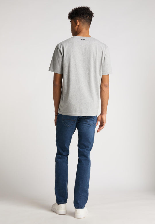 Ein Mann blickt von der Kamera weg und trägt das hellgraue Recaro  T-Shirt Spektrum, Bluejeans und weiße Sneakers im Retro-Look vor einem schlichten hellen Hintergrund.