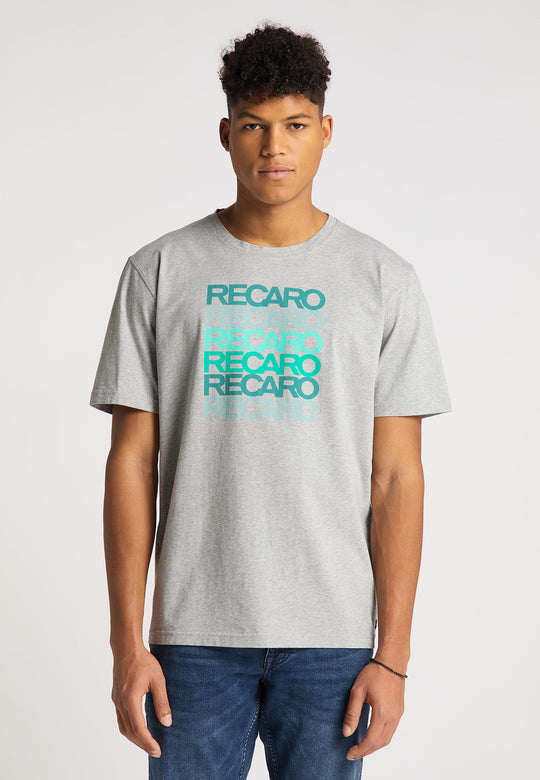 Ein junger Mann trägt das Recaro T-Shirt Spektrum in Hellgrau mit dem sich wiederholenden RECARO-Schriftzug in Blau und Türkis. Mit seinen kurzen, lockigen Haaren und Blue Jeans fällt er vor dem schlichten weißen Hintergrund auf.
