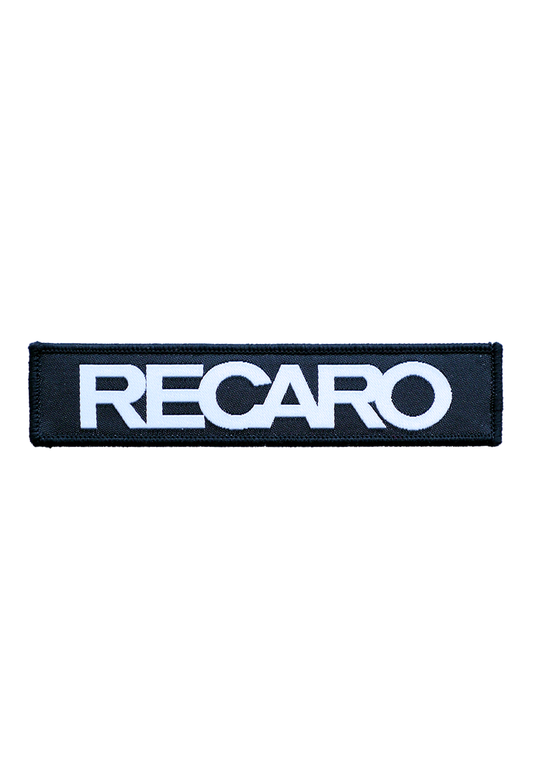 Der Patch RECARO 110x25mm von RECARO  ist ein rechteckiger schwarzer Patch aus strapazierfähigem Material, auf dem mittig das Wort RECARO in fetten, weißen Großbuchstaben steht.