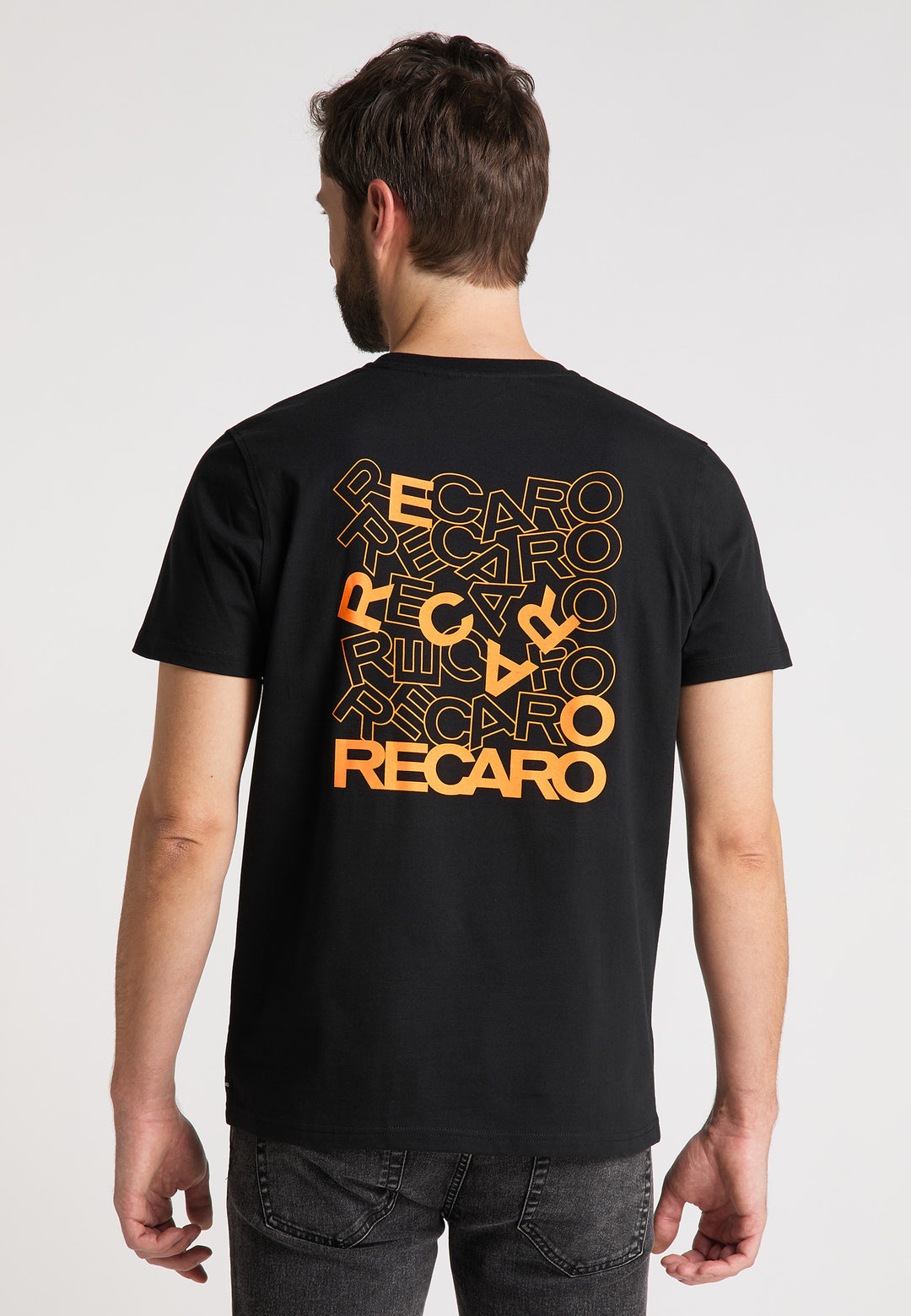 Ein Mann mit kurzen braunen Haaren, von hinten gesehen, trägt das RECARO T-Shirt Backprint mit mehreren überlappenden orangefarbenen RECARO-Logos auf der Rückseite, kombiniert mit dunklen Jeans.