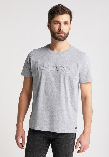 Ein Mann mit kurzen braunen Haaren und Bart trägt das RECARO T-Shirt Originals Embossed in Hellgrau mit einem 3D RECARO Logo auf der Brust, dazu schwarze Jeans und steht vor einem schlichten weißen Hintergrund.