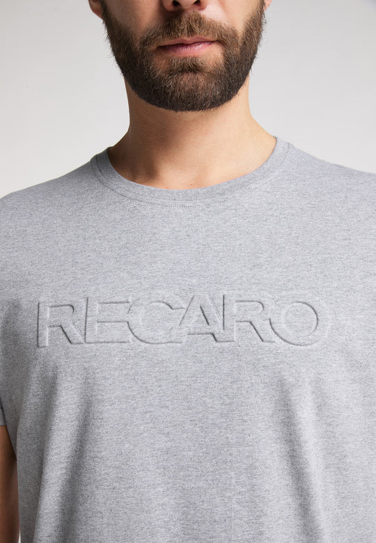Ein Mann mit gestutztem Bart trägt das RECARO T-Shirt Originals Embossed, ein hellgraues T-Shirt aus 100 % Baumwolle mit einem auffälligen 3D-RECARO-Logo auf der Brust. Auf dem Bild sind nur seine untere Gesichtshälfte und sein Oberkörper zu sehen.