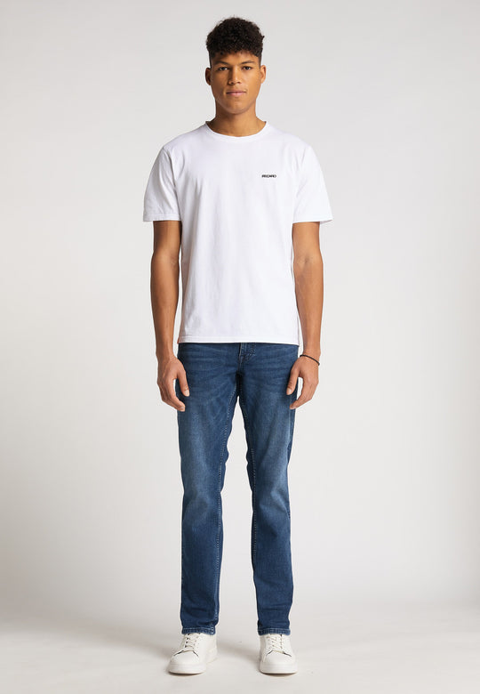 Ein junger Mann blickt nach vorne und trägt ein locker sitzendes Recaro_Merch_Daniel T-Shirt Originals Basic, Bluejeans und weiße Turnschuhe vor einem schlichten hellen Hintergrund.