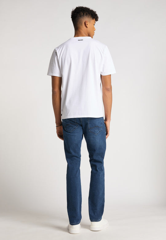 Ein junger Mann steht mit dem Rücken zur Kamera und trägt ein locker sitzendes T-Shirt Originals Basic von Recaro, Bluejeans und weiße Turnschuhe vor einem hellgrauen Studiohintergrund.