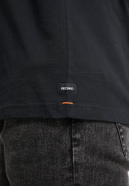 Nahaufnahme des unteren Rückens einer Person, die das T-Shirt Originals Basic von Recaro_Merch_Daniel trägt, ein schwarzes T-Shirt mit lockerer Passform, einem kleinen RECARO-Label und orangefarbenen Nähten, kombiniert mit verwaschenen schwarzen Jeans.