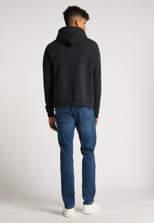 Eine Person steht mit dem Rücken zur Kamera und trägt einen Hoodie Originals Basic von Recaro, kombiniert mit Blue Jeans und weißen Sneakers vor einem schlichten hellen Hintergrund.