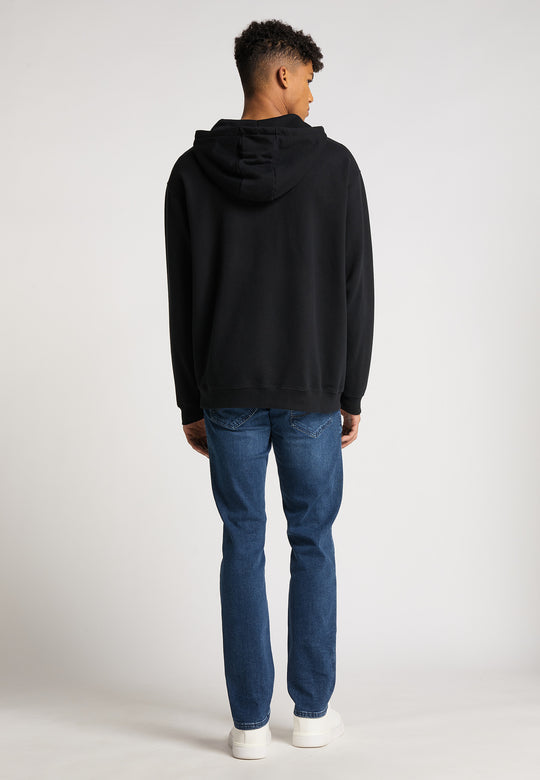 Eine Person steht mit dem Rücken zur Kamera und trägt eine schwarze Recaro Hoodiejacke Originals, Blue Jeans und weiße Sneakers vor einem schlichten hellen Hintergrund.
