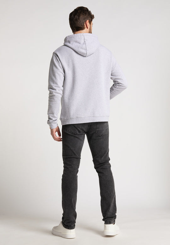 Ein Mann blickt von der Kamera weg und trägt einen hellgrauen Hoodie Originals Basic von RECARO, dunkelgraue Jeans und weiße Turnschuhe vor einem schlichten hellen Hintergrund.