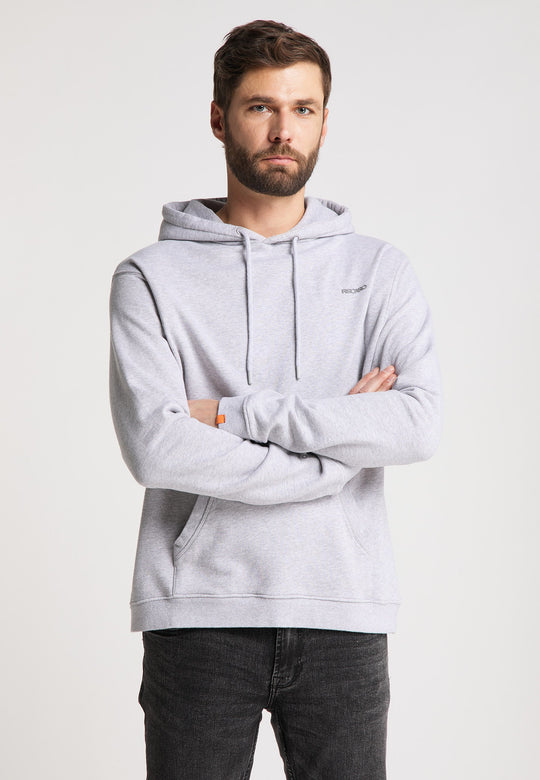 Ein Mann mit Bart und kurzen Haaren steht mit verschränkten Armen nach vorne gerichtet da und trägt einen locker sitzenden Recaro Hoodie Originals Basic und dunkle Jeans vor einem schlichten hellen Hintergrund.
