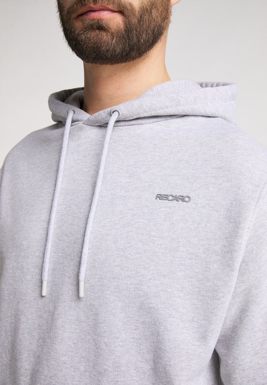 Ein Mann trägt den hellgrauen Recaro_Merch_Daniel Hoodie Originals Basic mit Kordelzug und lockerer Passform. Aus weicher Baumwolle gefertigt und mit dezenter Stickerei auf der Brust versehen, verleiht der Hoodie dezenten Stil. Sein bärtiges Gesicht ist teilweise sichtbar.