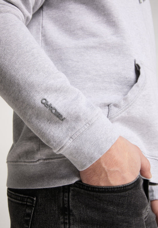 Eine Person trägt einen hellgrauen Hoodie Originals Basic von Recaro_Merch_Daniel mit der Aufschrift „Recyclo“ auf dem Ärmel, dazu schwarze Jeans und eine Hand in der weichen Baumwolltasche.