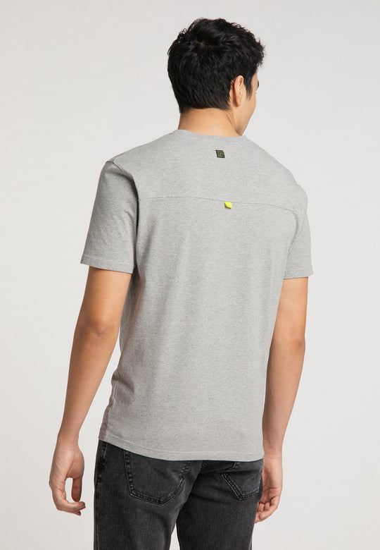Eine Person blickt von der Kamera weg und trägt das hellgraue Recaro_Merch_Daniel T-Shirt Performance mit Performance-Print-Logo und dunkle Jeans. Der lockere Schnitt ist vor einem schlichten, hellen Hintergrund zu sehen.