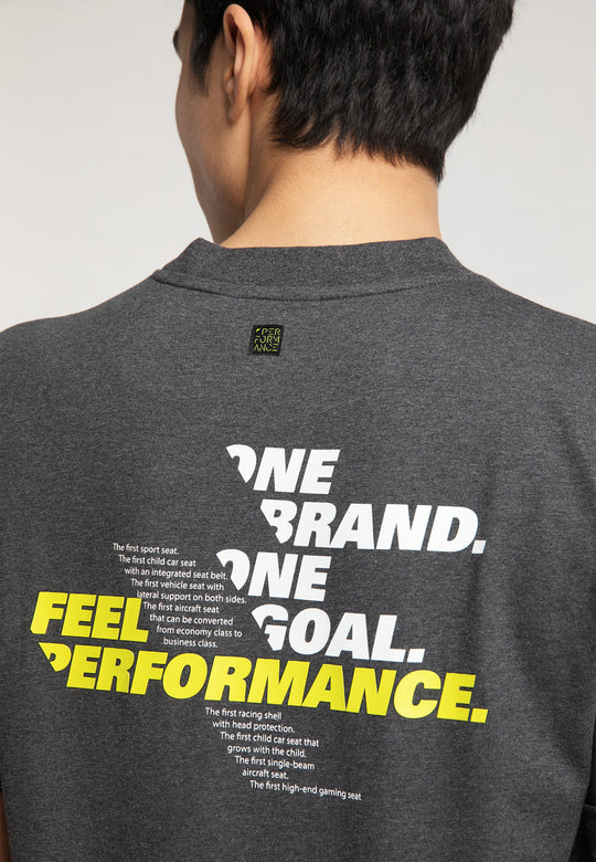 Eine Person trägt das RECARO T-Shirt „One Brand One Goal“ in Dunkelgrau mit dem fettgedruckten weiß-gelben Text „ONE BRAND. ONE GOAL. FEEL PERFORMANCE.“ und einem kleineren weißen „RECARO Premium-Gaming-Seat“-Logo auf der Rückseite.