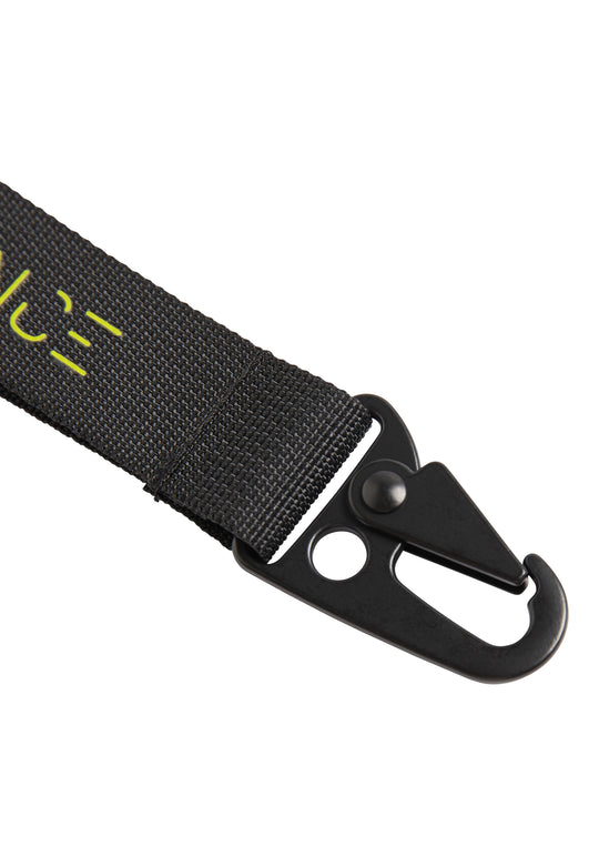Nahaufnahme des RECARO Key Clip Performance: ein schwarzes Stoffband mit einem Karabinerverschlusshaken aus Metall mit zwei runden Löchern und teilweise sichtbaren gelben Markierungen auf dem Band.