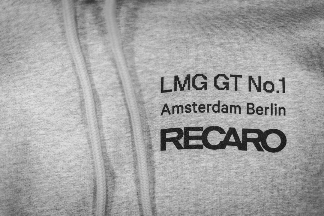 Nahaufnahme des LMG x RECARO Hoodies von Recaro mit dem schwarzen Text „LMG GT No.1 Amsterdam Berlin RECARO“ auf grauem Stoff, sichtbaren Kordeln und zur Feier der Verbindung des LMG Racing Club zur GT4 European Series.