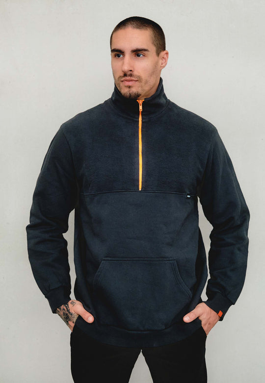 Ein Mann mit kurzen Haaren und gestutztem Bart trägt das Recaro_Merch_Daniel Half Zip Sweatshirt Originals im dunklen Design mit leuchtend orangefarbenem Reißverschluss und Fronttasche – ideal fürs Outdoor-Training oder als vielseitige Freizeitkleidung.