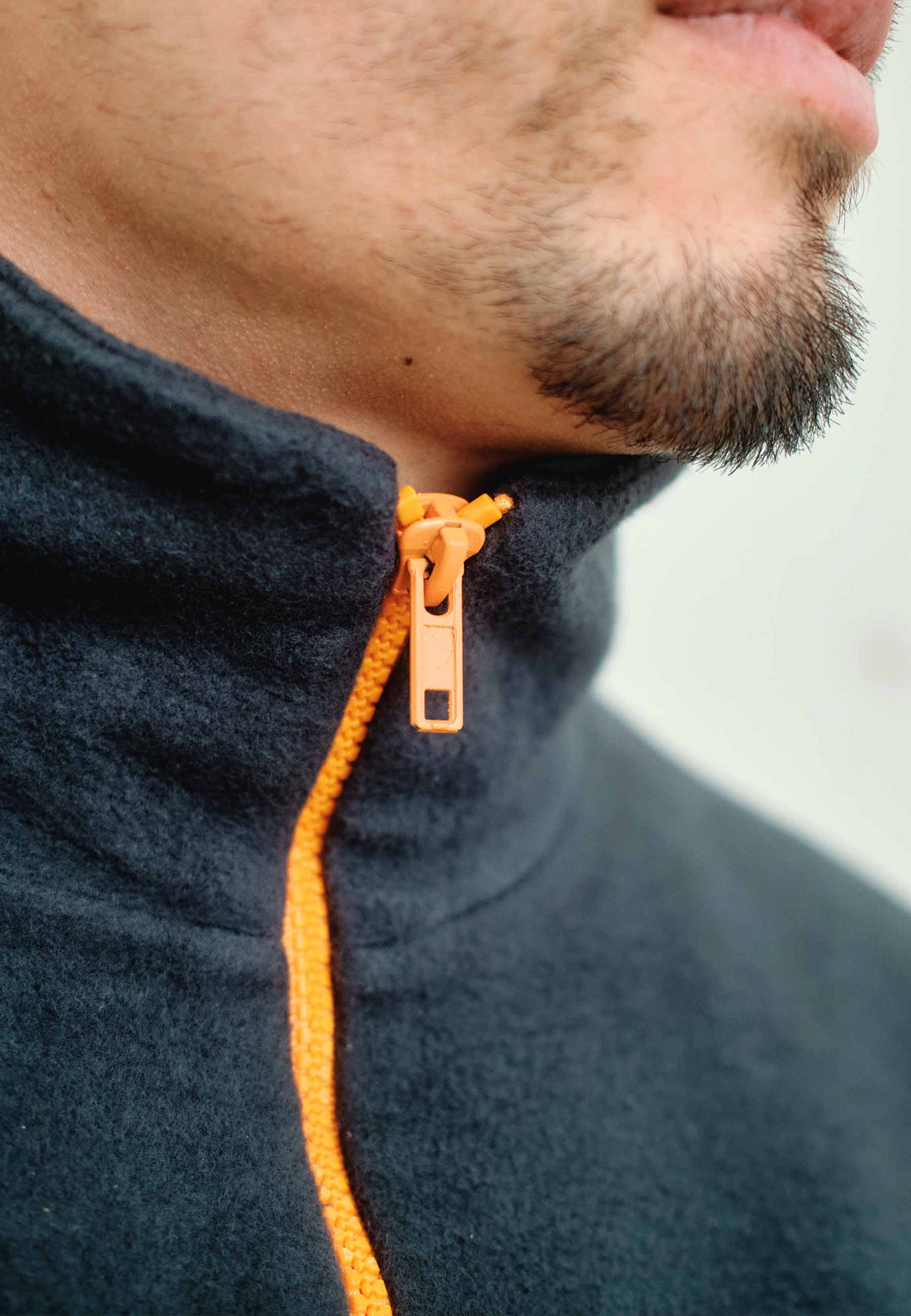 Nahaufnahme des unteren Gesichts und Halses eines Mannes, der das Recaro_Merch_Daniel Half Zip Sweatshirt Originals in dunkler Farbe mit orangefarbenem Reißverschluss trägt, der teilweise bis zum Kinn hochgezogen ist; leichter Gesichtshaaransatz sichtbar – ideal für Outdoor-Training oder stylische Freizeitkleidung.
