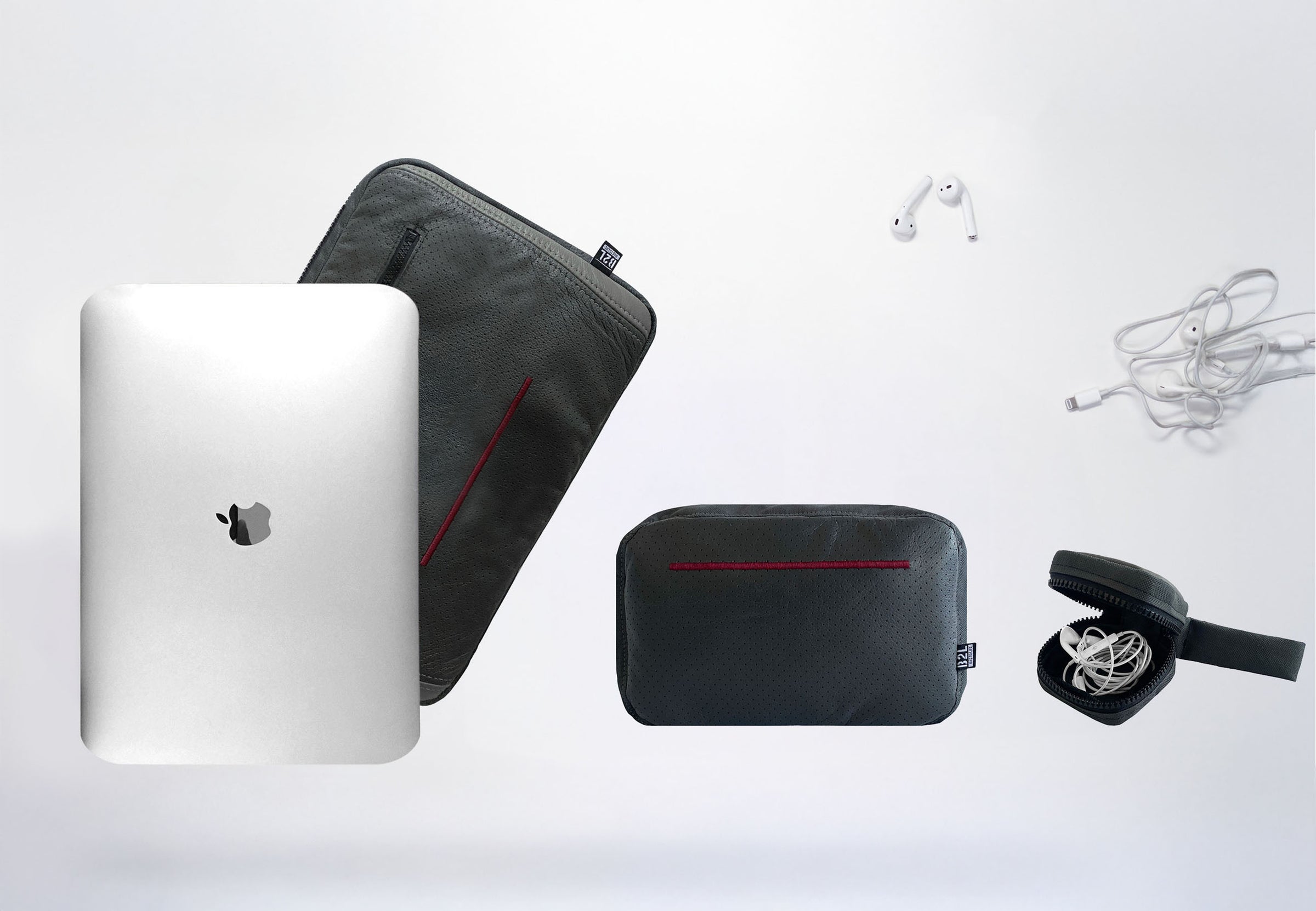 Ein silbernes MacBook, eine schwarze Laptophülle, eine schwarze Tasche mit Reißverschluss, ein Paar weiße kabellose Ohrhörer und ein kleines Etui mit kabelgebundenen Ohrhörern sind auf einer weißen Oberfläche angeordnet.
