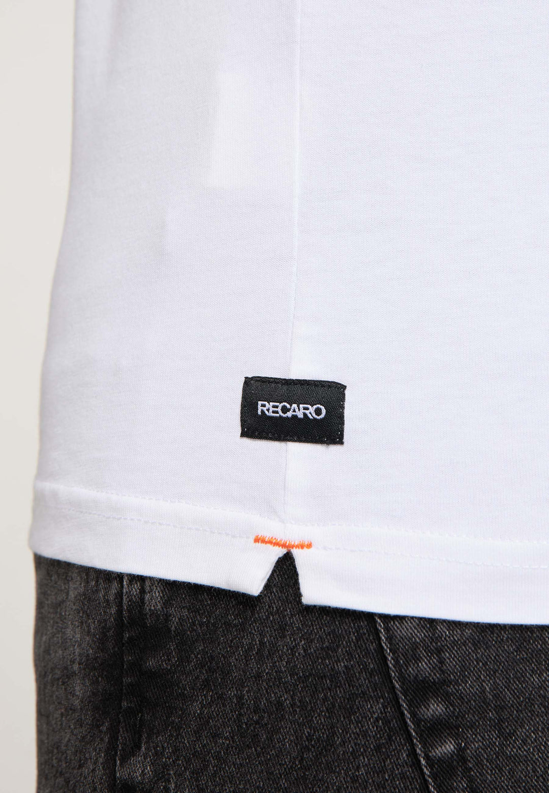 Nahaufnahme des RECARO T-Shirts Gradient in Weiß mit dezentem Farbverlauf, orangefarbenem Saumstich und kleinem schwarzen RECARO Label. Kombiniert mit dunklen Jeans.