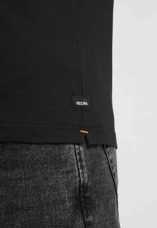 Nahaufnahme einer Person, die das RECARO T-Shirt Gradient in Schwarz mit einem kleinen schwarzen RECARO-Label am Saum trägt, kombiniert mit schwarzen Jeans vor einem schlichten hellen Hintergrund.