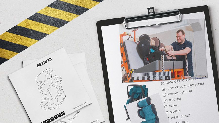 Auf einem Tisch liegt ein Klemmbrett mit dem Foto eines Mannes, der einen Kindersitz einstellt, neben Diagrammen und Papieren zu Kindersitzen. In der Nähe sind auf dem Boden gelb-schwarze Warnstreifen zu sehen.