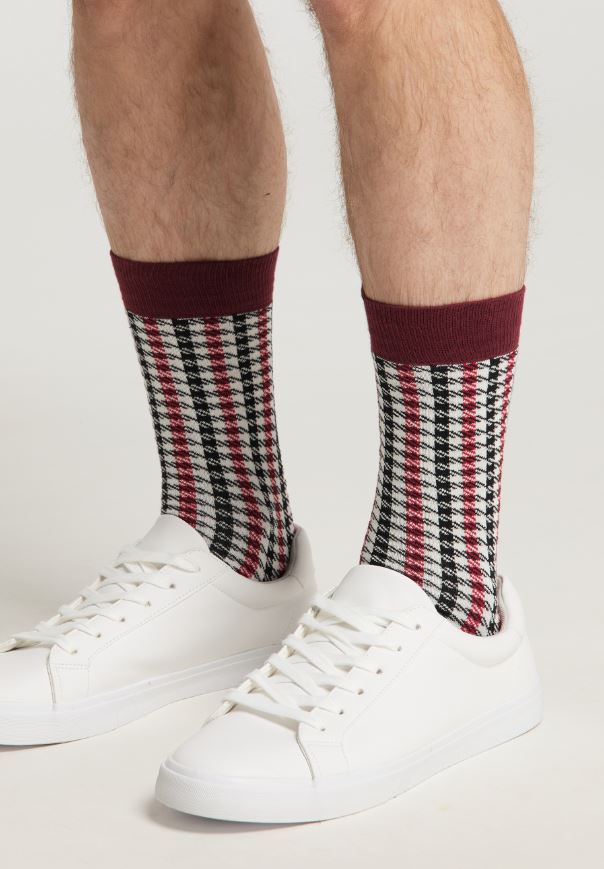 Eine Person trägt weiße Sneakers und Recaro_Merch_Daniel Socken Pepita, nur Unterschenkel und Füße sind vor einem schlichten Hintergrund zu sehen, was einen stylischen Look ergibt.