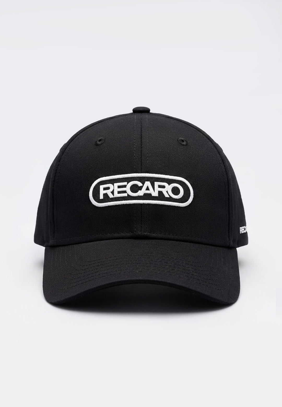 Die Baseball Cap Basic black von RECARO Shop ist aus 100% Baumwolle, mit weißem RECARO-Schriftzug im ovalen Rahmen vorn. Sie verfügt über einen verstellbaren Verschluss für individuelle Passform und wird vor hellem Hintergrund präsentiert.