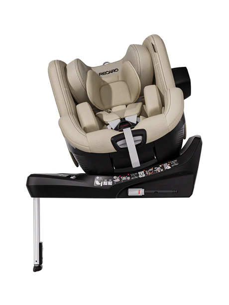 Der RECARO Shop TORON 1 ist ein beigefarbener, ergonomisch geformter Kindersitz, der auf einer schwarzen, verstellbaren Basis mit Stützfuß montiert ist. Er verfügt über gepolsterte Seiten, eine Kopfstütze, Sicherheitsgurte und eine sichtbare Anleitung auf der Basis.