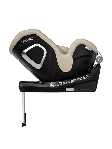Der schwarz-beigefarbene RECARO Shop TORON 1 Kindersitz in der Seitenansicht ist mit Sicherheitsetiketten, einer ergonomischen Liegefläche, einer 360°-Drehung für leichten Zugang und einem Stützfuß für den sicheren Einbau im Fahrzeug ausgestattet.