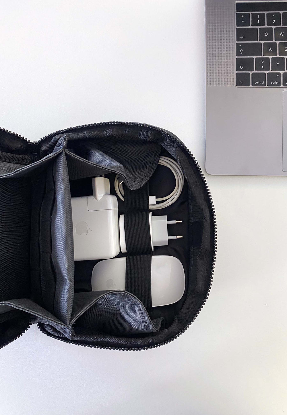 Der RECARO Shop Tech & Travel Organizer aus echtem RECARO-Sitzleder bietet Platz für Ladegeräte und Kabel und liegt auf einer weißen Oberfläche neben einer silbernen Laptop-Tastatur.