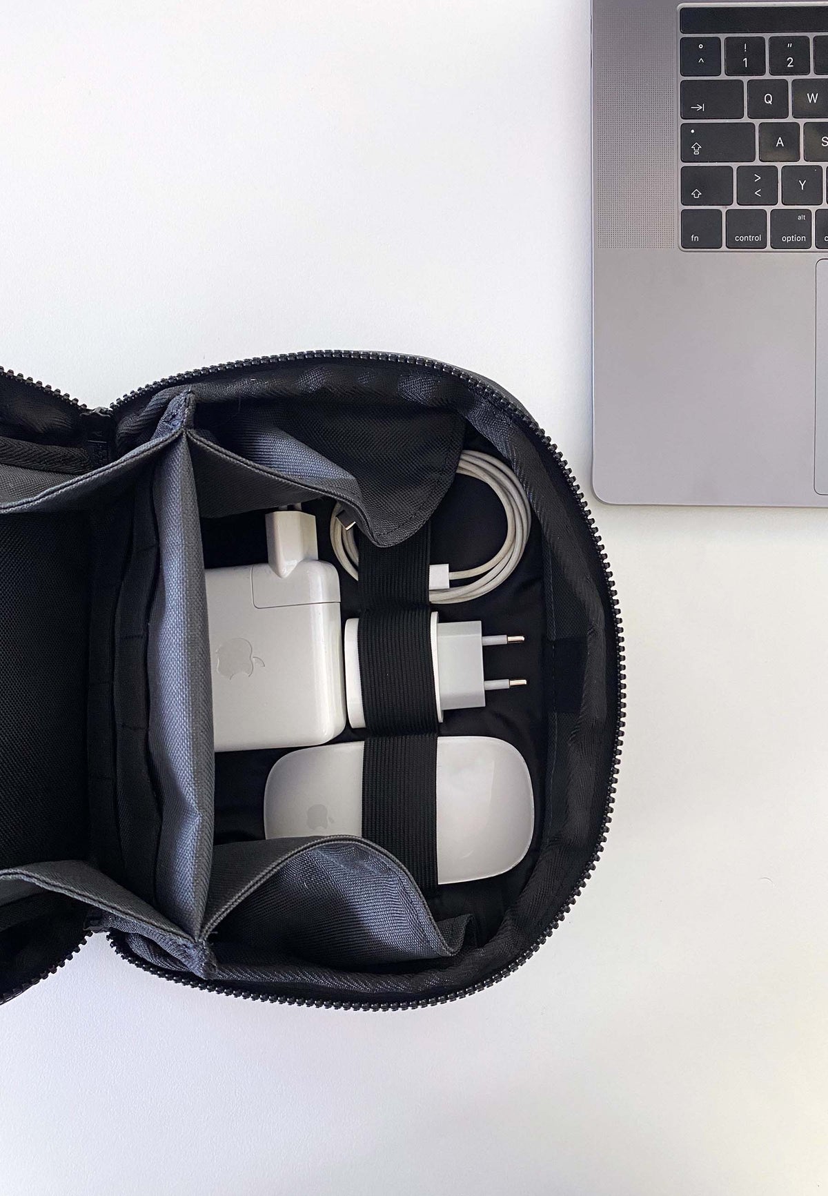 Der RECARO Shop Tech & Travel Organizer aus echtem RECARO-Sitzleder bietet Platz für Ladegeräte und Kabel und liegt auf einer weißen Oberfläche neben einer silbernen Laptop-Tastatur.