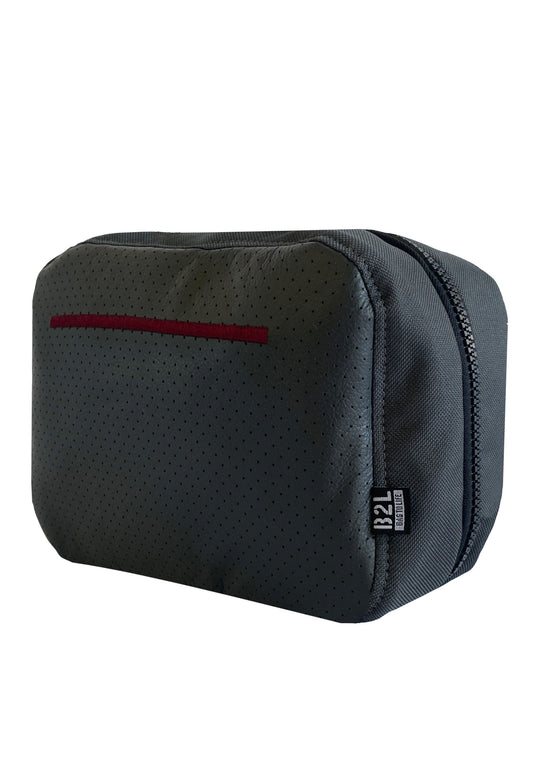 Der RECARO Shop Tech & Travel Organizer ist eine dunkelgraue Kulturtasche aus RECARO-Sitzleder mit dezentem Lochmuster, kastanienbrauner Akzentlinie, Reißverschluss oben und kleinem schwarzen B2L-Etikett – ideal zum Organisieren Ihrer wichtigsten Dinge.