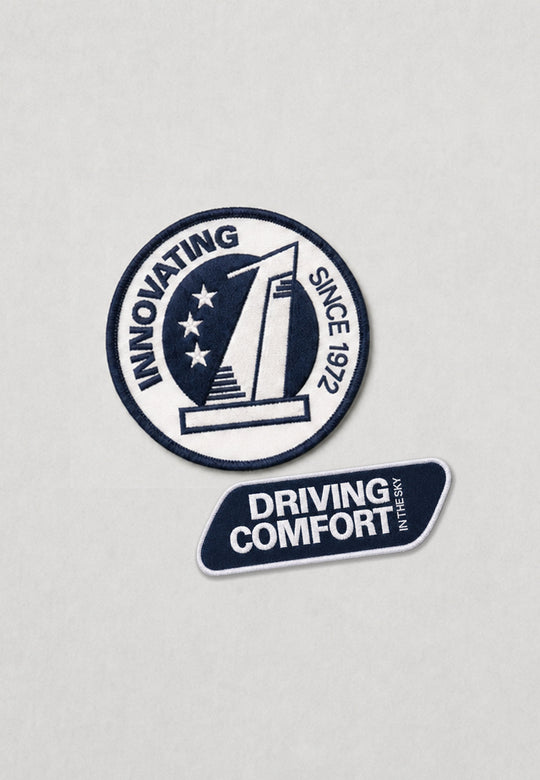 Zwei gestickte Aufnäher: ein runder mit "INNOVATING SINCE 1972" und einem stilisierten Gebäude, der andere blau mit "DRIVING COMFORT INTENSIVELY" - perfekte Akzente für Ihre marinefarbene Pilotenjacke RECARO aus dem RECARO Shop.