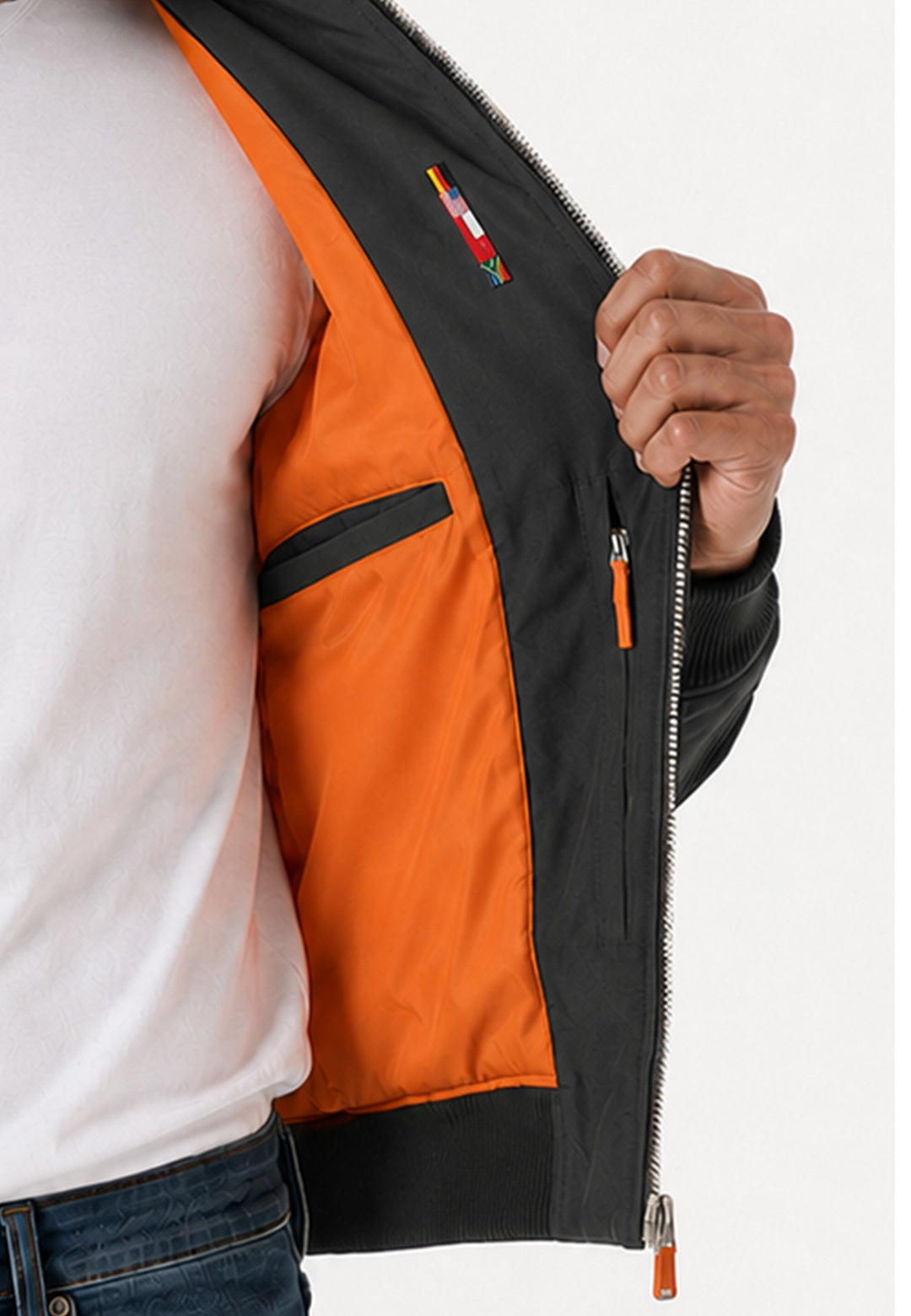 Eine Person in weißem Hemd und blauen Jeans hält die „Racing Jacke RECARO, anthrazit“ aus dem RECARO Shop offen und gibt den Blick frei auf das leuchtend orangefarbene Futter und die Innentasche mit Reißverschluss in klassischer Bomber-Silhouette.