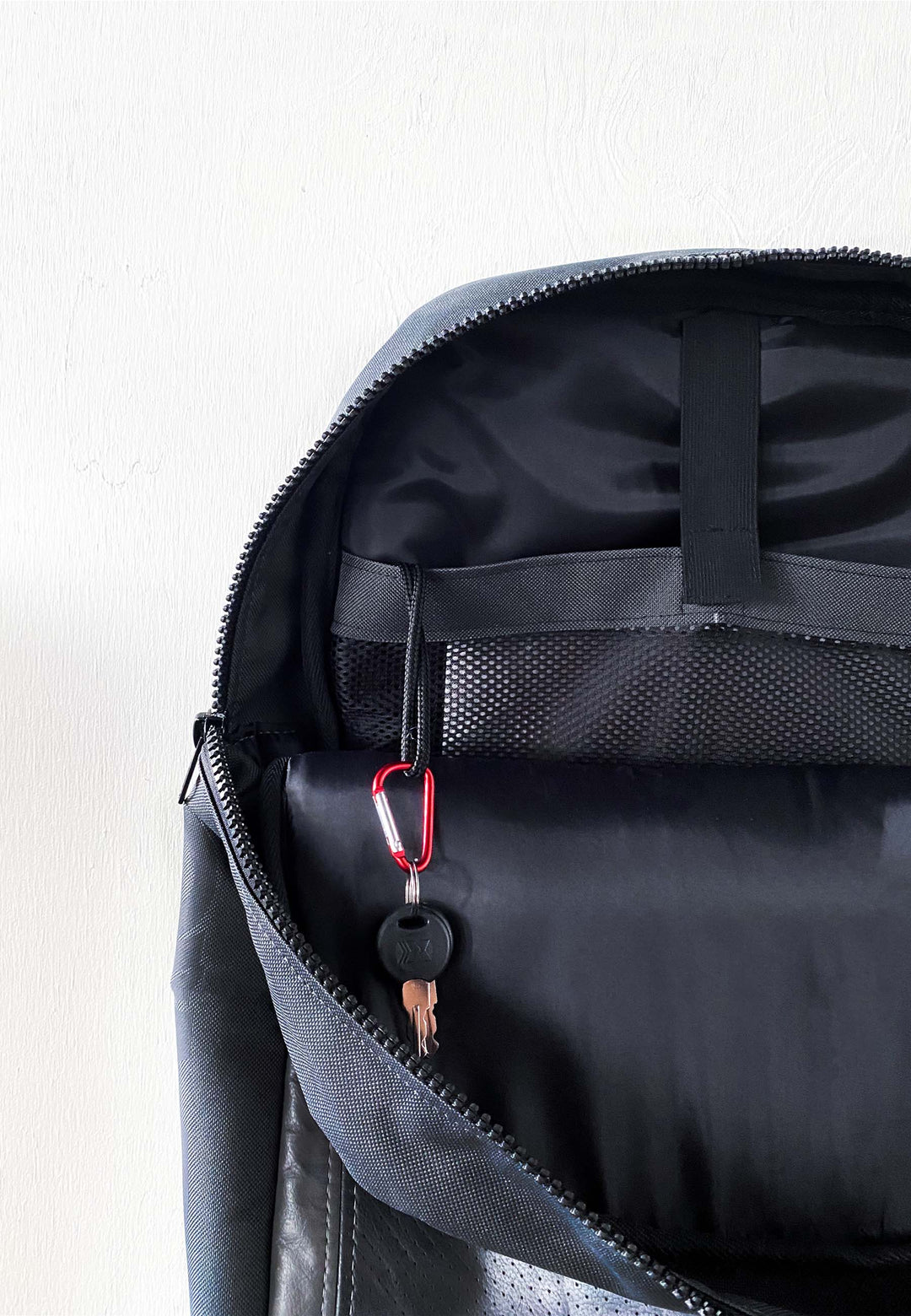 Eine Nahaufnahme eines geöffneten RECARO Shop Travel & Tech Rucksacks zeigt einen Schlüsselbund an einem roten Karabiner in einer kleinen Innentasche mit sicherem Laptopfach, alles vor einem schlichten weißen Hintergrund.