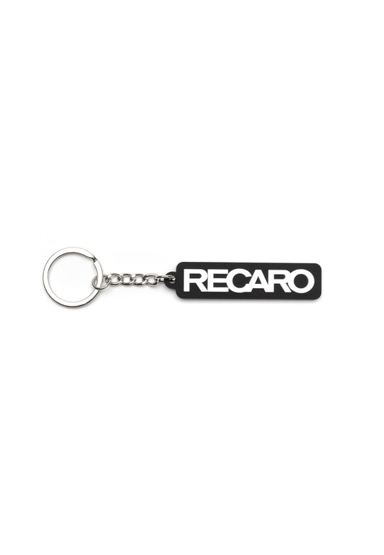 Der Schlüsselanhänger Originals RECARO aus dem RECARO Shop ist ein schwarzer, rechteckiger Gummischlüsselanhänger mit auffälligem weißem Schriftzug, der mit einer kurzen Kette an einem silbernen Schlüsselring befestigt ist und für sportlichen Style sorgt.