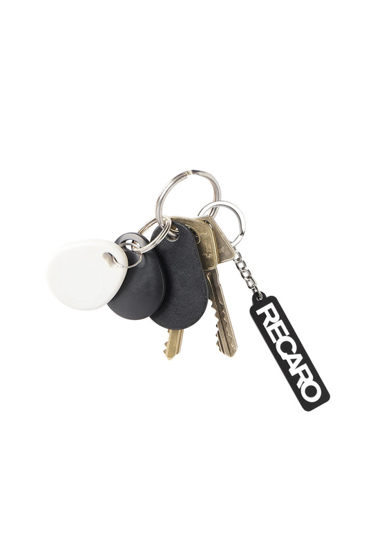 Ein Set aus zwei Metallschlüsseln mit schwarzen Kunststoffköpfen, einem weißen Schlüsselanhänger und dem Schlüsselanhänger Originals RECARO by RECARO Shop im sportlichen Stil, alles auf einem silbernen Schlüsselring vor weißem Hintergrund.