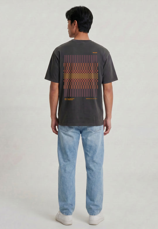 Eine Person steht mit dem RECARO Shop T-Shirt Spektrum Backprint in dunkelgrau (garment washed) mit rotem und orangefarbenem geometrischem Rückendesign, gepaart mit hellblauen Jeans und weißen Turnschuhen vor einem schlichten hellen Hintergrund.