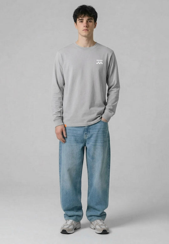 Eine junge Person steht vor einem schlichten grauen Hintergrund. Sie trägt das RECARO Shop Longsleeve Checkered Shirt, eine locker sitzende Bluejeans und graue Turnschuhe. Eine Hand steckt in der Hosentasche, die andere ruht an der Seite.